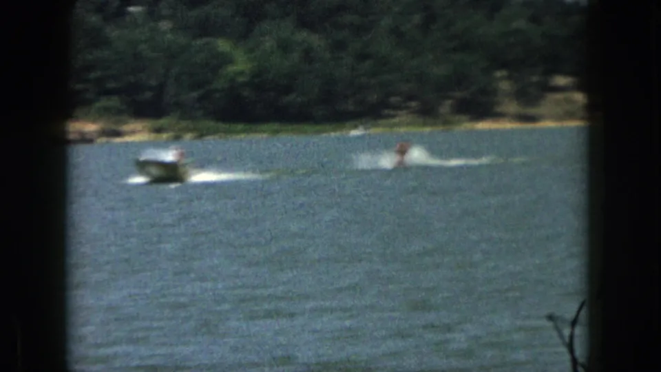 Soft 8mm frame from 1961 Michigan showing a boat pulling a distant water skier across rippled lake water.
