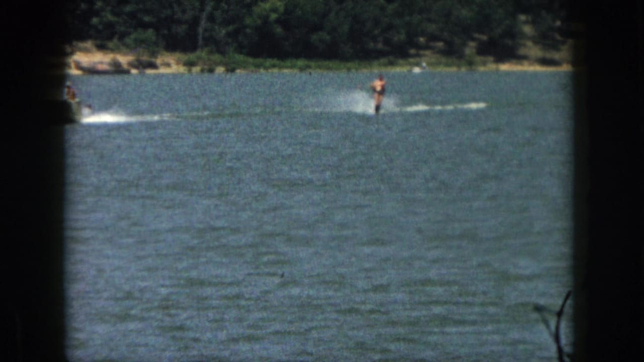 Distant man water skiing on open lake water with a wake behind him.
