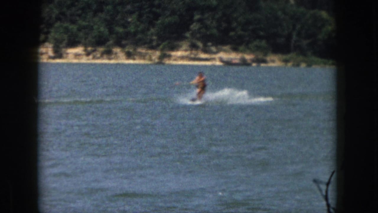 Water skier moving across open lake water with white spray and trees along the far shore.