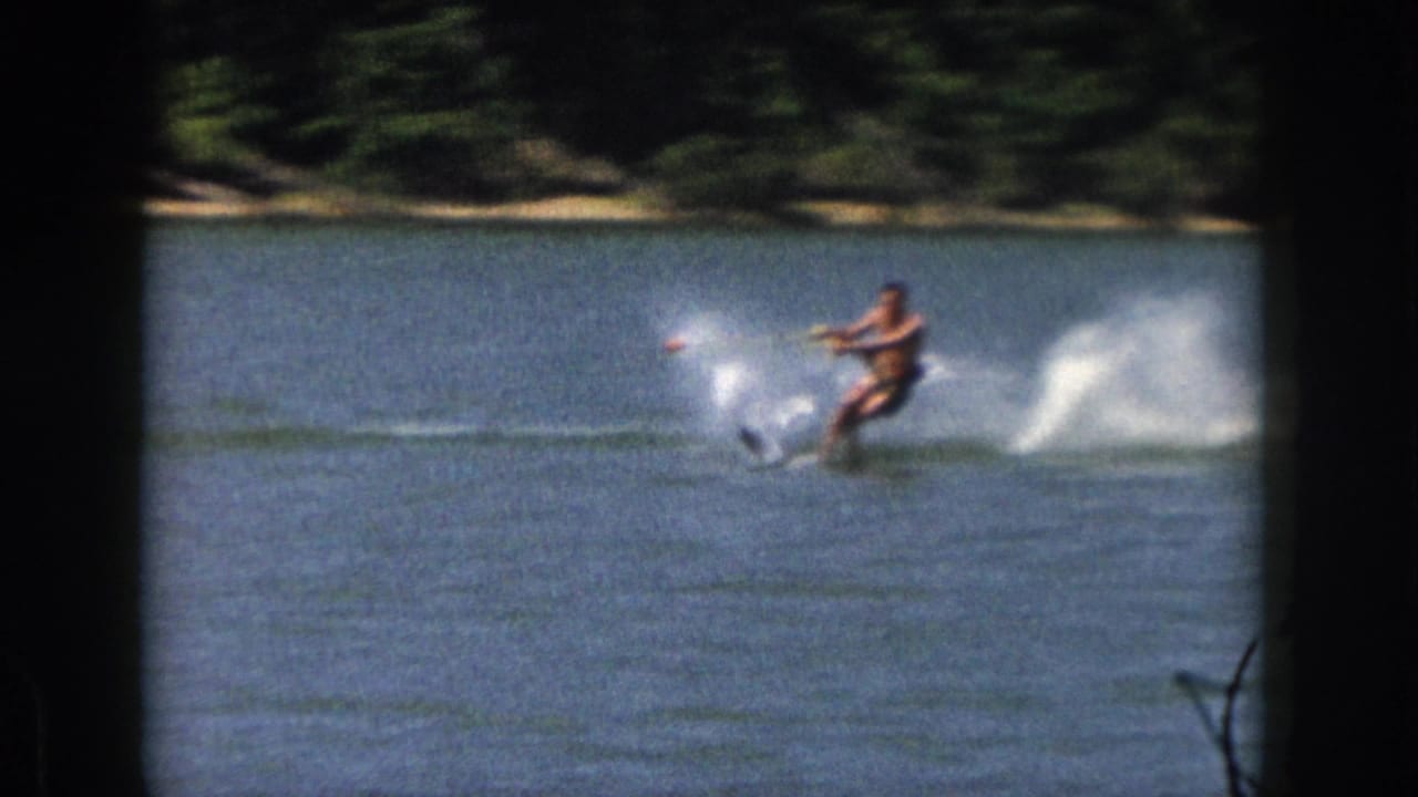 A water skier turns on the lake, pulling a wake and white spray near the far shore.
