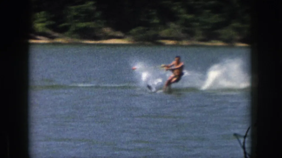 1961 Michigan lake footage shows a water skier leaning through a turn, with tow rope visible and spray breaking across the water.
