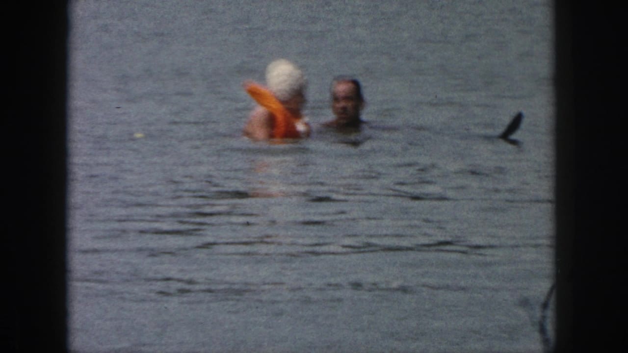 1961 Michigan 8mm frame showing a man and a woman in lake water, the woman wearing a white swim cap and orange float.
