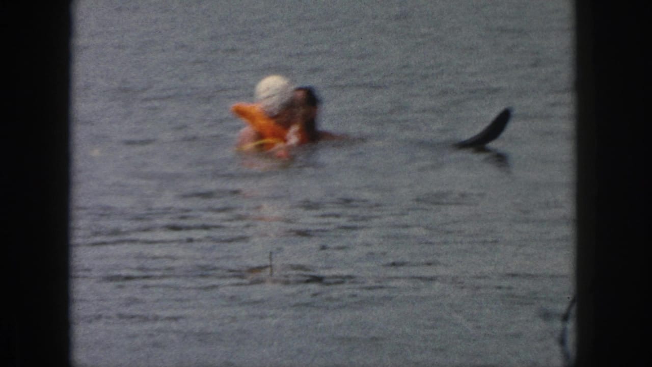 A woman in a white swim cap and orange float leans near a man in lake water.