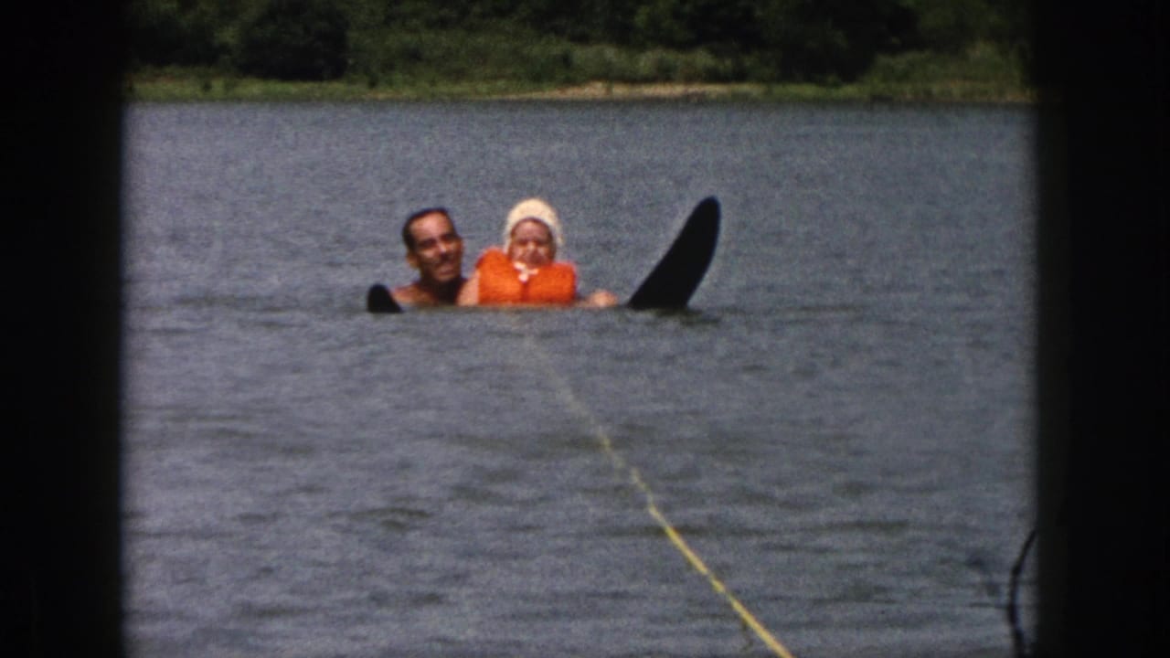 1961 Michigan 8mm frame of a father and daughter floating in lake water near a black water ski and yellow tow rope.