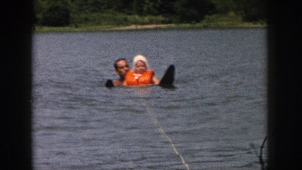 Two people face the camera while floating in the lake, with a black water ski beside them.