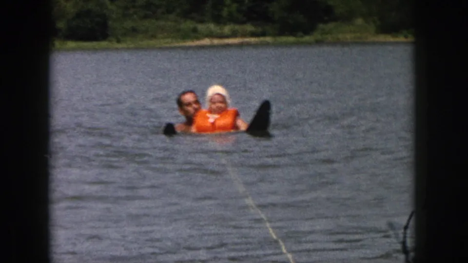 1961 Michigan home-movie frame showing a father and daughter floating together on a lake near a visible water ski.