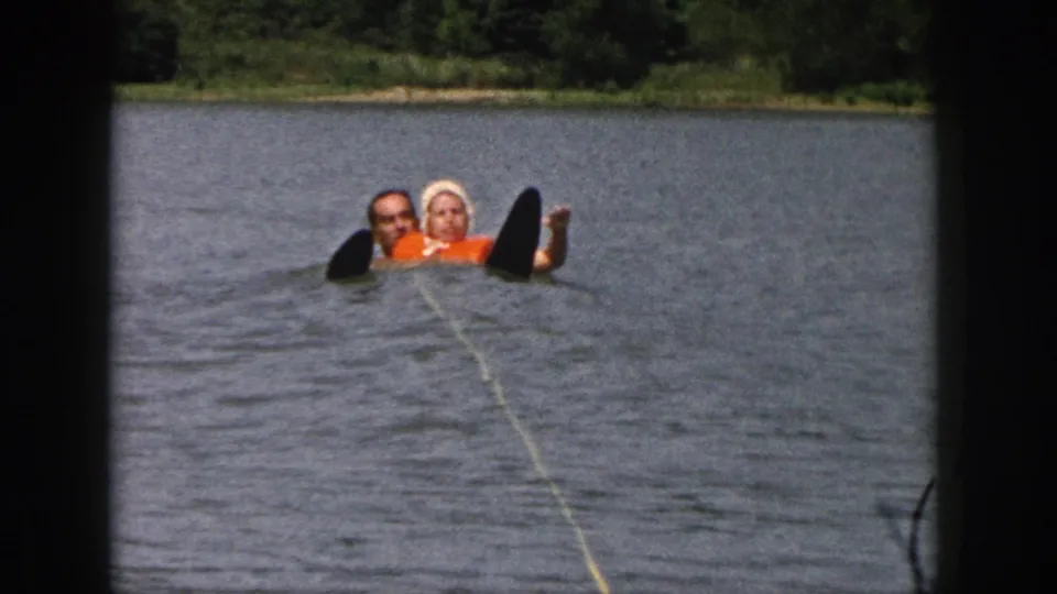 1961 Michigan 8mm frame of a father and daughter in lake water, with the tow rope and water ski suggesting water-ski activity.