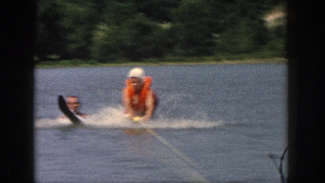 A person in an orange life vest is pulled across the lake with water skis visible.