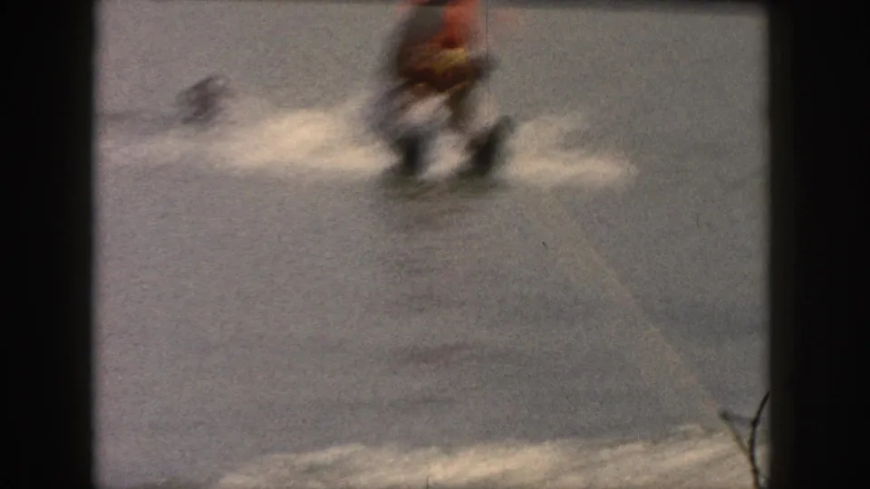 A soft, blurry 8mm frame shows the skier moving across the Michigan lake with spray and a tow rope visible.