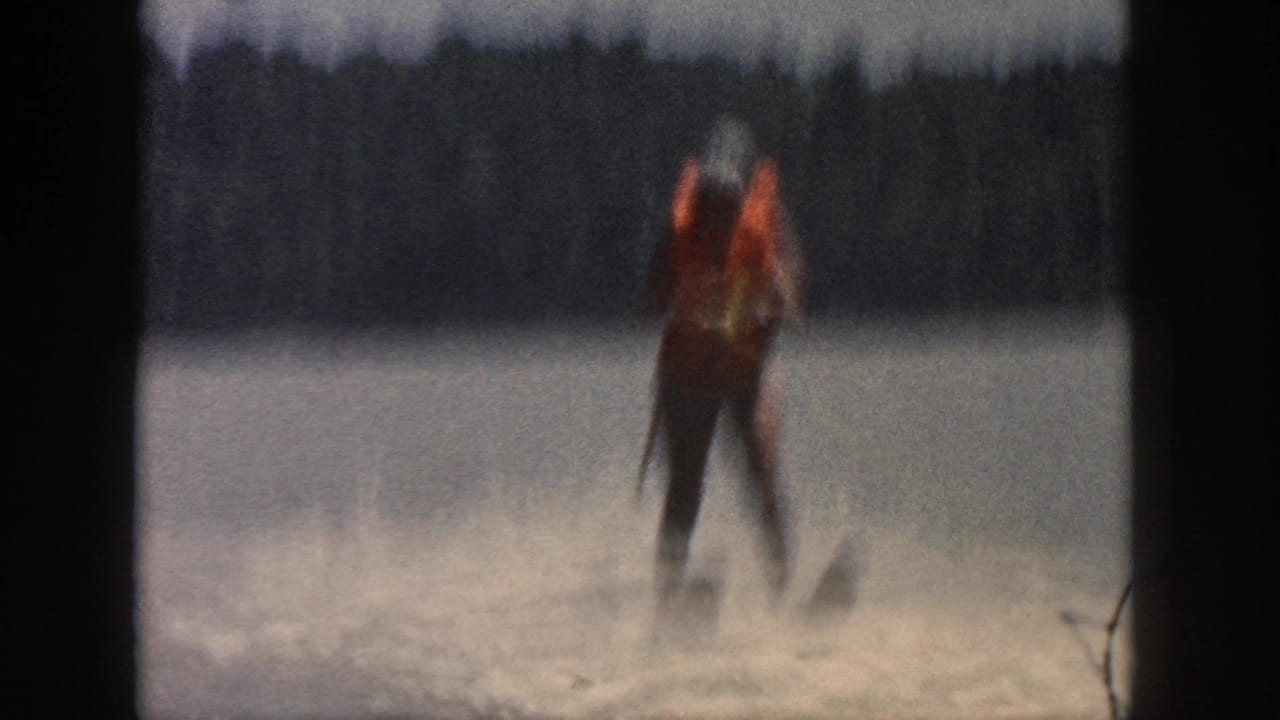 Blurred water skier stands upright on the lake amid spray and distant trees.