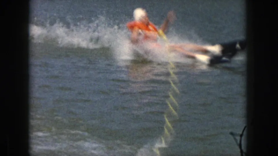 The woman in the orange life vest appears to fall sideways while water skiing, sending spray across the Michigan lake surface.