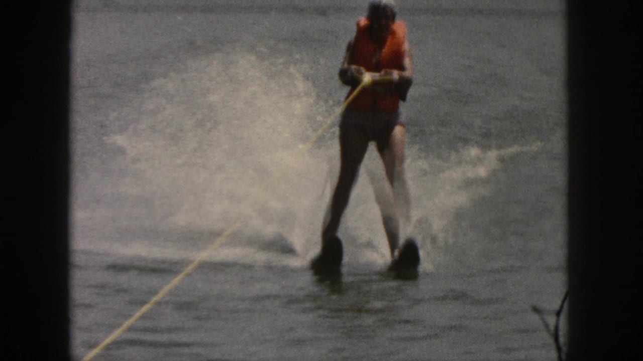 Water skier leans back on two skis with spray rising behind them.