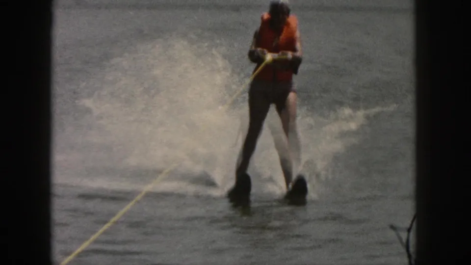 Water skier on a Michigan lake in 1961, wearing an orange life vest and holding a yellow tow rope as water sprays behind.