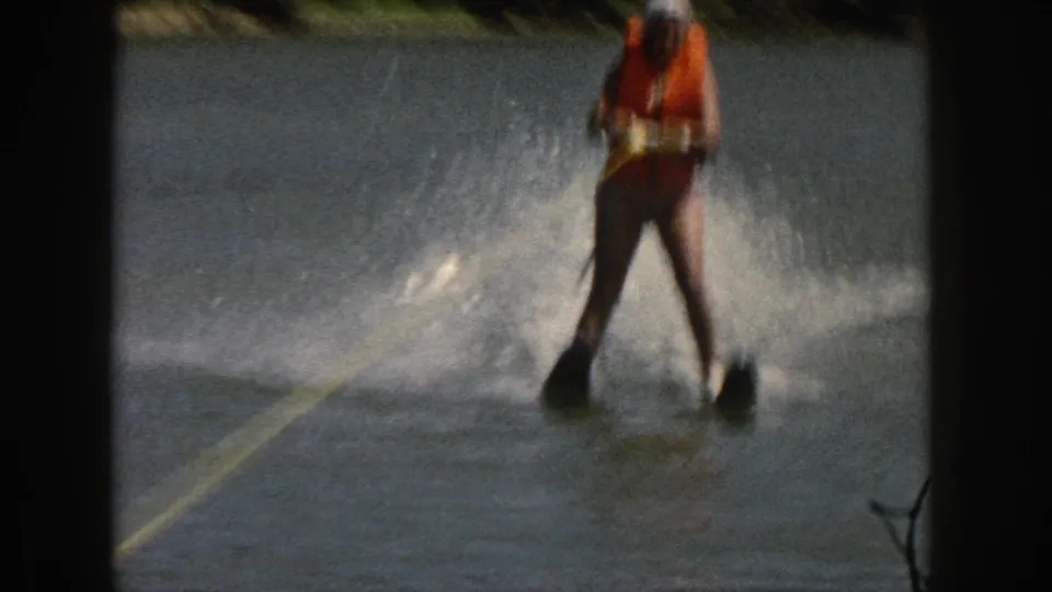 1961 Michigan 8mm still of a water skier in an orange life vest moving across a lake, with tow rope and spray visible.