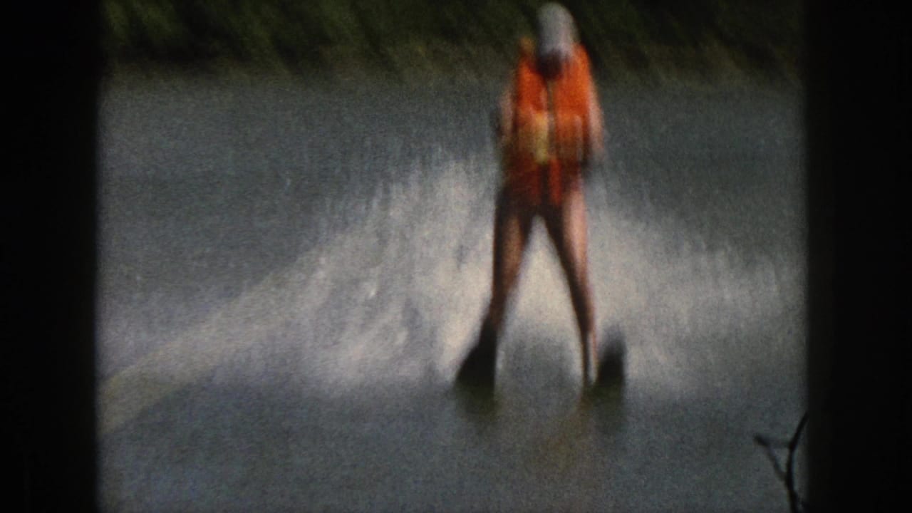 1961 Michigan 8mm frame showing a water skier in an orange life vest gliding on a river with heavy spray and dark film borders.