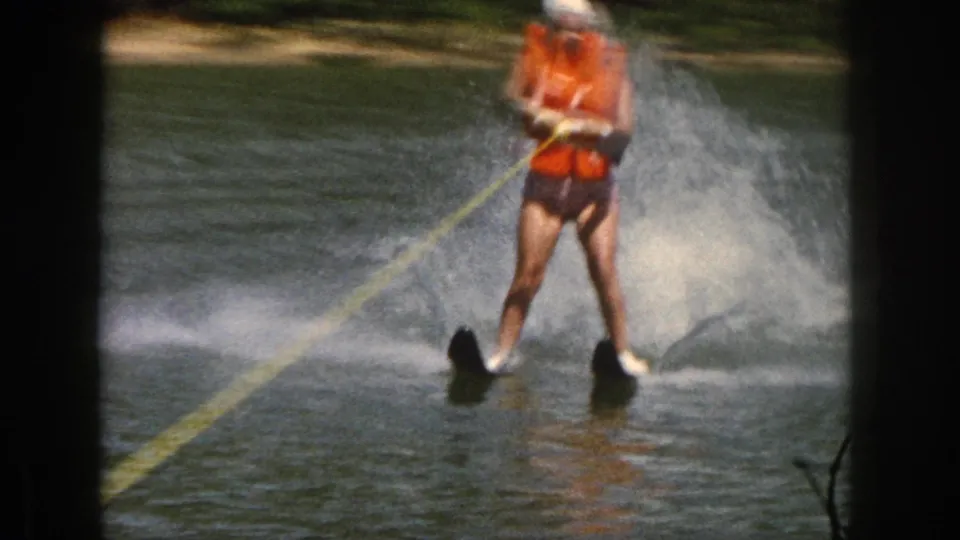 Soft 8mm frame from Michigan in 1961 showing a water skier centered on the river, holding the tow handle as spray rises behind.