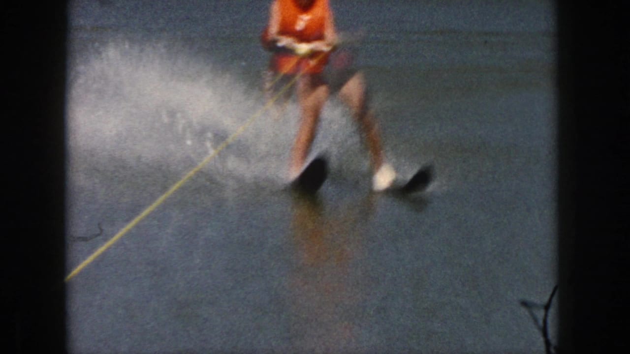 Water skier rides toward the camera with spray behind one ski.