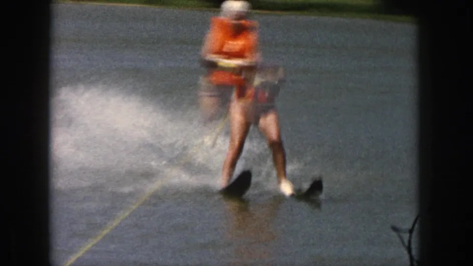 1961 Michigan frame showing a water skier leaning on twin skis, with a yellow tow rope and spray visible across the lake.