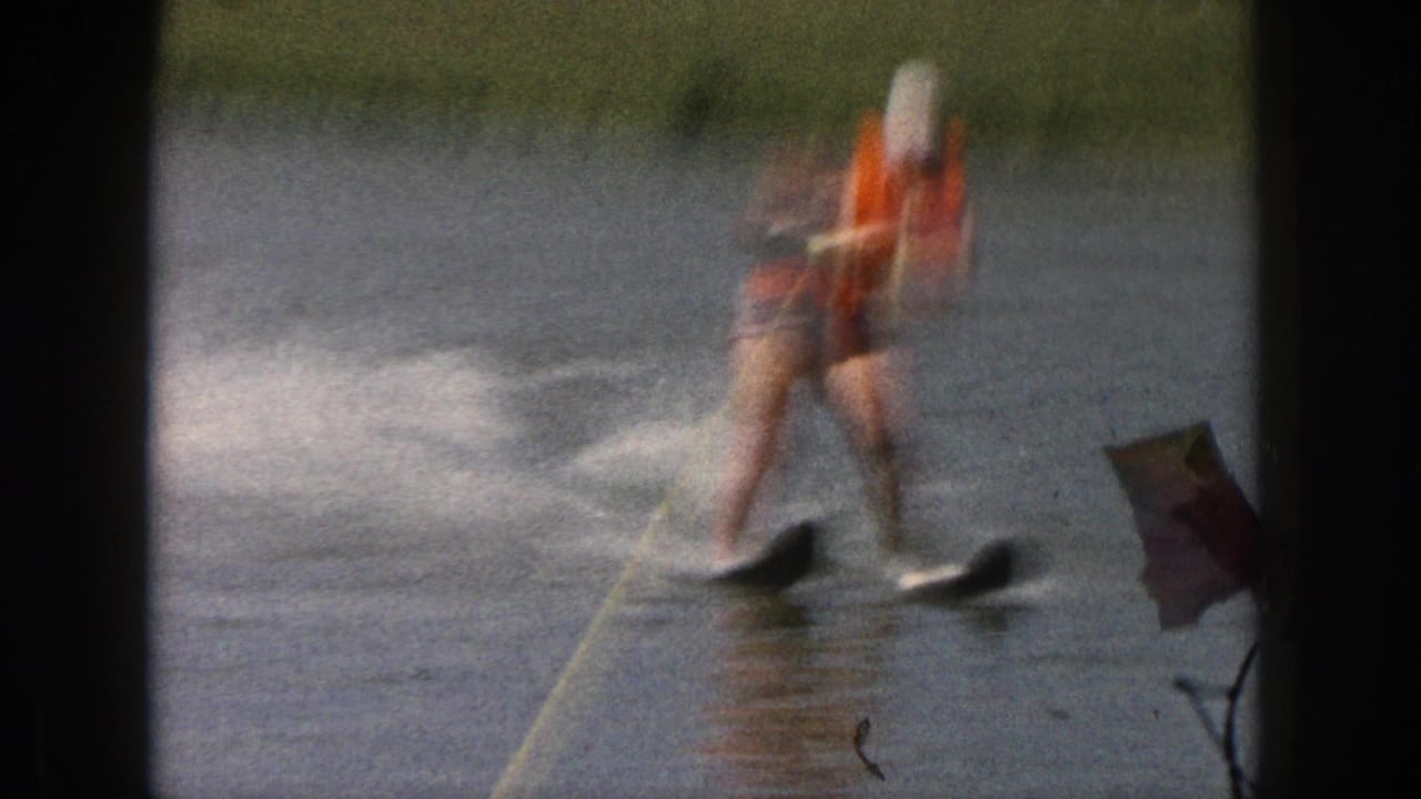 1961 Michigan 8mm frame showing a skier on dark water skis with a yellow tow rope visible over the lake.