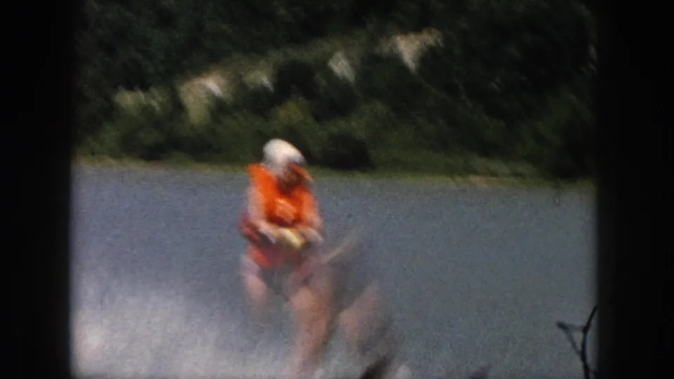 1961 Michigan home-movie frame of a water skier crossing the lake with trees visible along the shore.
