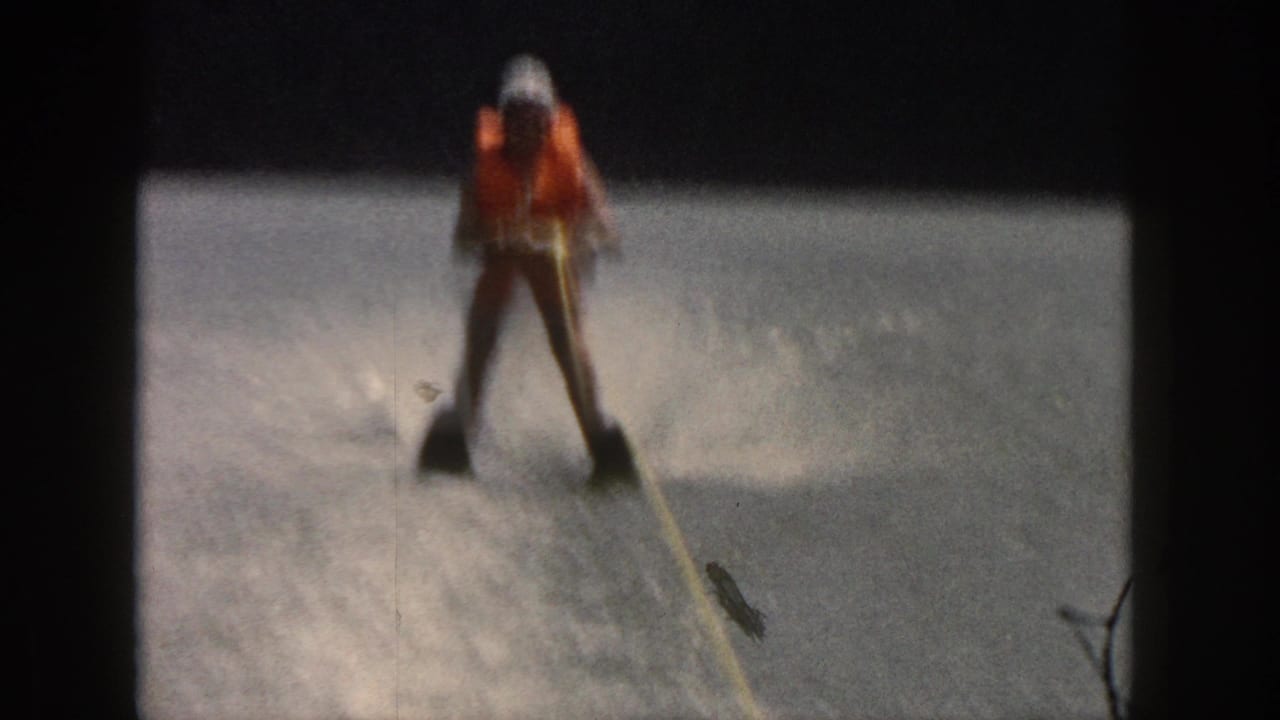 1961 Michigan home-movie frame showing the skier upright behind a tow rope with river spray in the background.