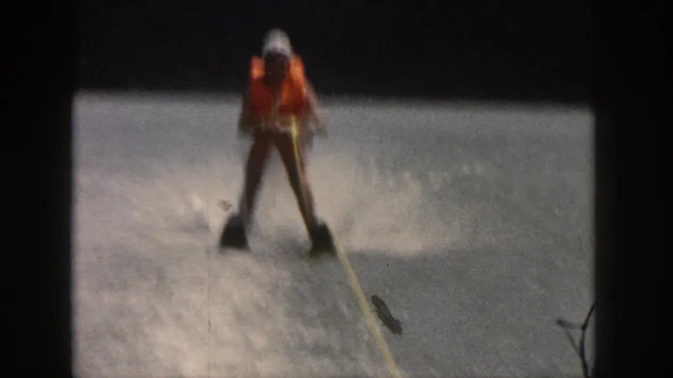 1961 Michigan home-movie frame showing the skier upright behind a tow rope with river spray in the background.