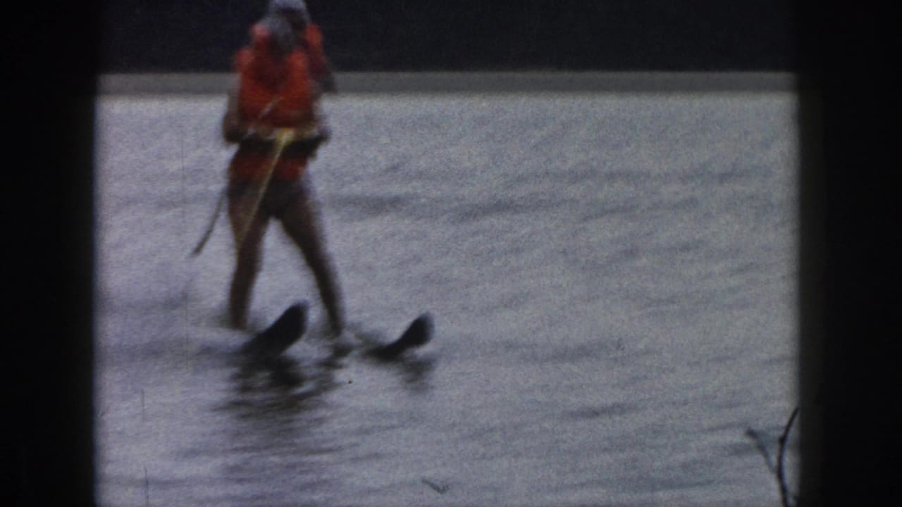 1961 Michigan 8mm frame showing a distant water skier in an orange life vest and white swim cap moving across a lake.
