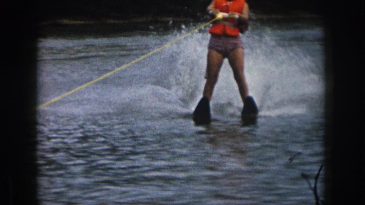 Woman in an orange life preserver water skis through spray while holding a yellow tow rope.