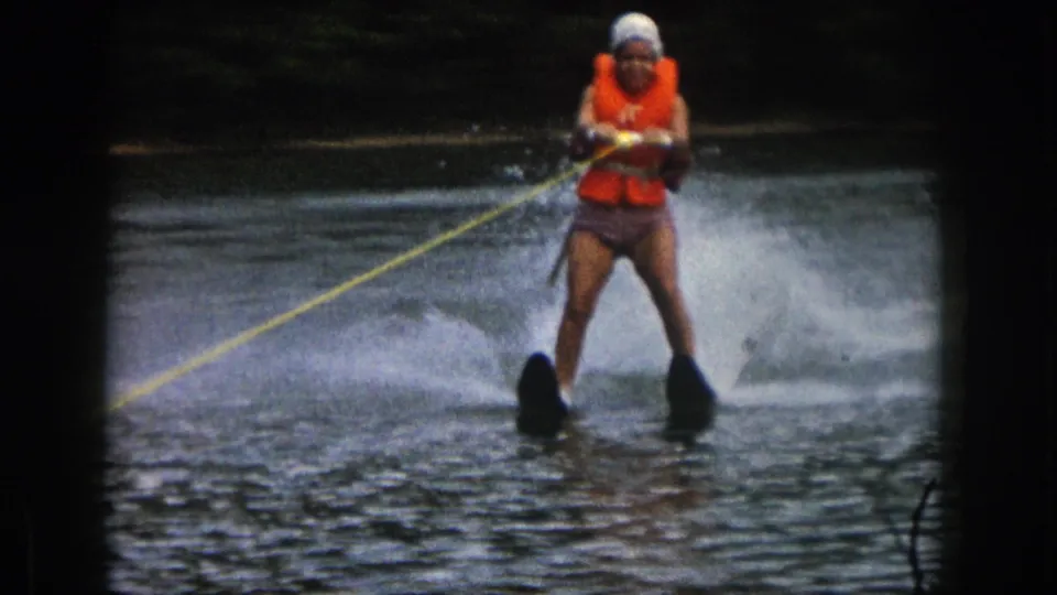 1961 Michigan 8mm frame showing a woman in an orange life preserver water skiing toward the camera on a lake.
