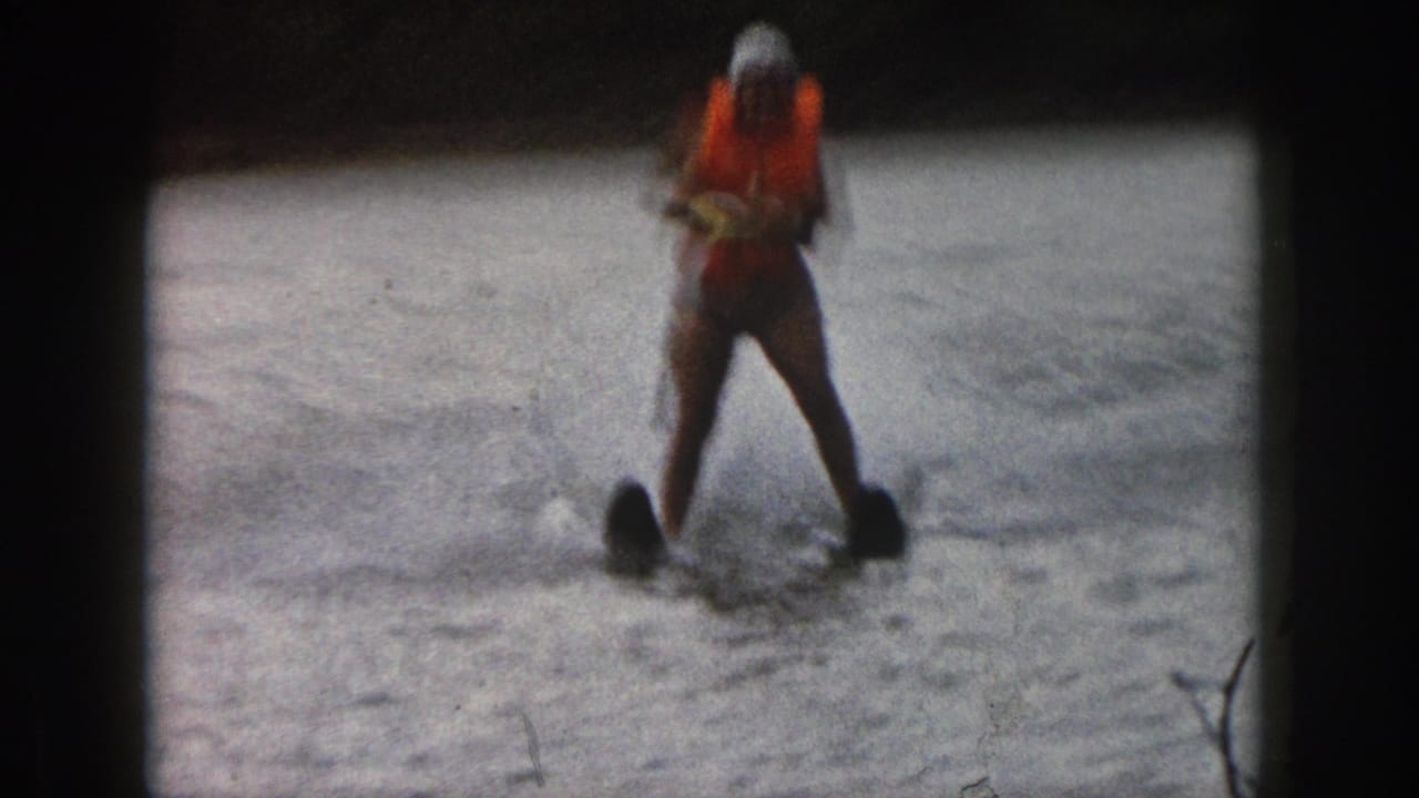 Water skier in an orange life vest glides over choppy lake water.