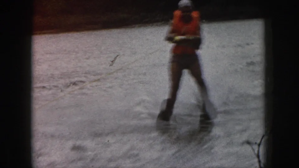 Soft 1961 Michigan home-movie frame showing the water skier leaning forward on skis over the lake surface.