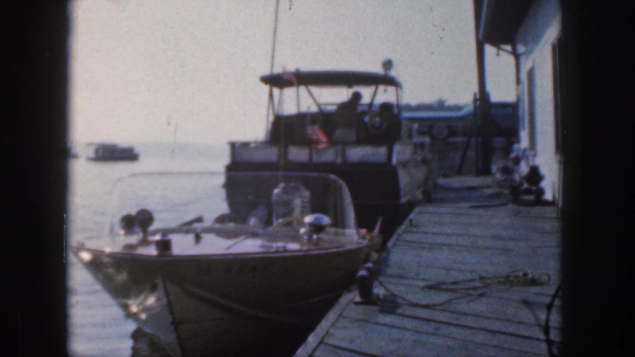 Small speedboat moored in front of a larger cabin cruiser beside a wooden pier.