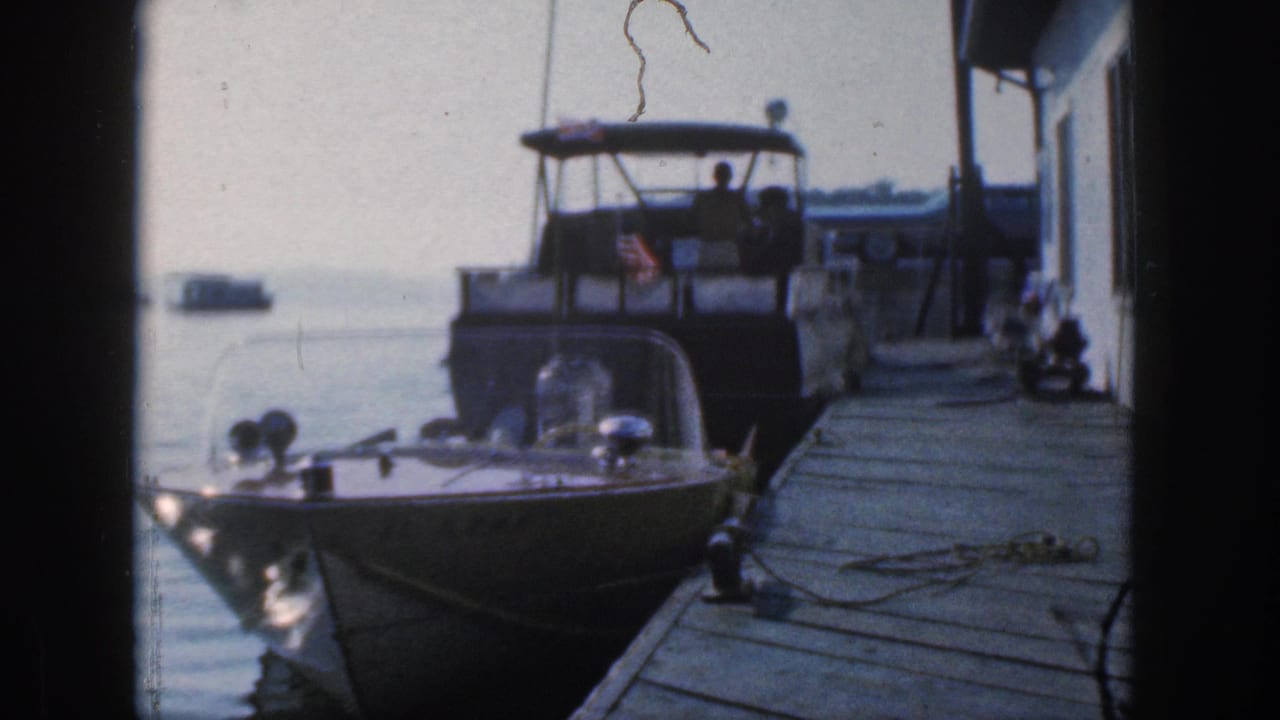 Cabin cruiser and foreground speedboat tied along a wooden dock with water beyond.