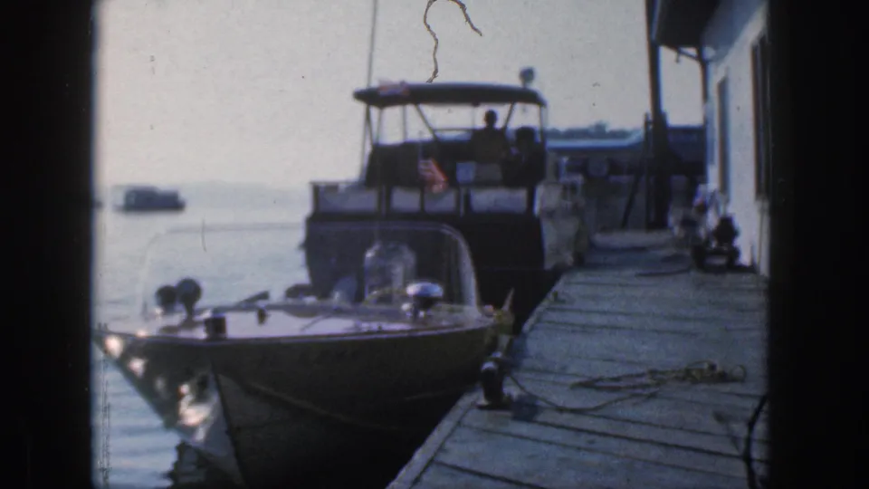 Dockside 8mm view of motorboats in Michigan, with a cabin cruiser, foreground speedboat, flag, and distant boats on the water.