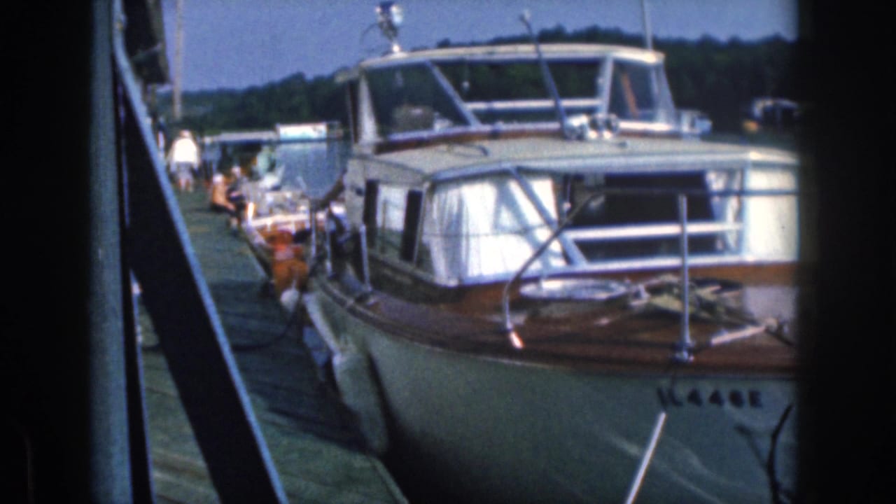 Motorboat bow and windshield seen from the dock with boats and people behind it.