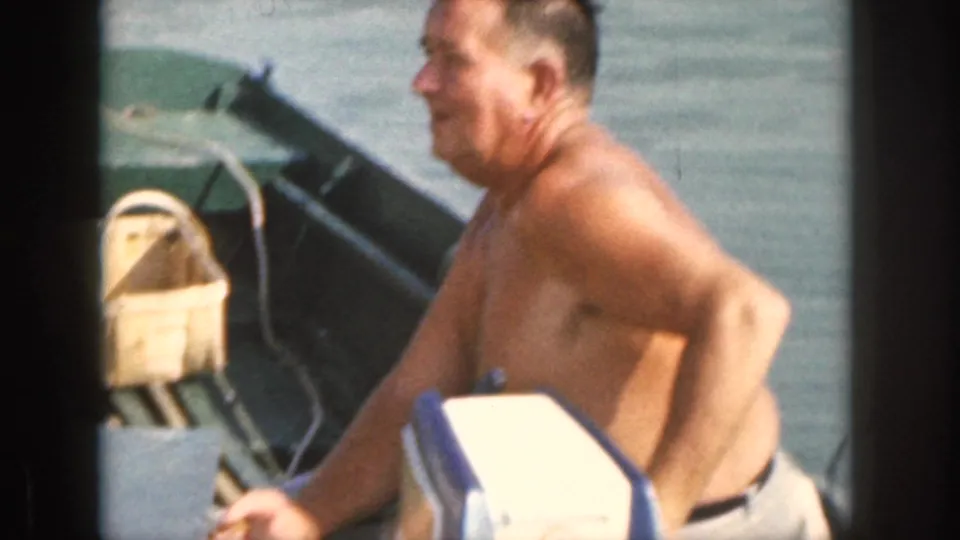 A shirtless man appears to work near a small outboard motor on a boat deck in 1961 Michigan home-movie footage.