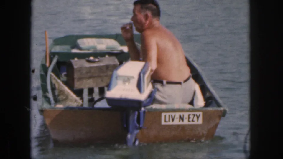 A side view shows the shirtless man in the small Michigan motorboat, with an outboard motor, oar, wood box, and LIV-N-EZY plate.