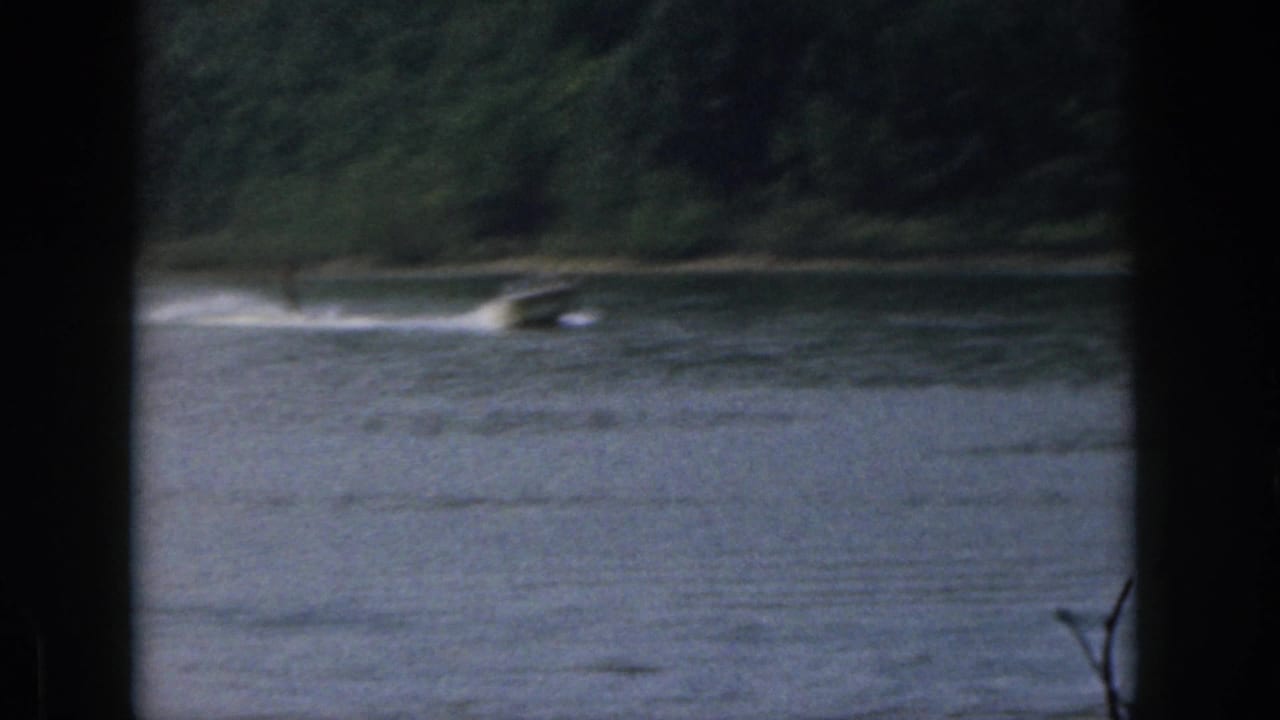 1961 Michigan lake view with a small distant boat or tow wake moving near a tree-lined shoreline.