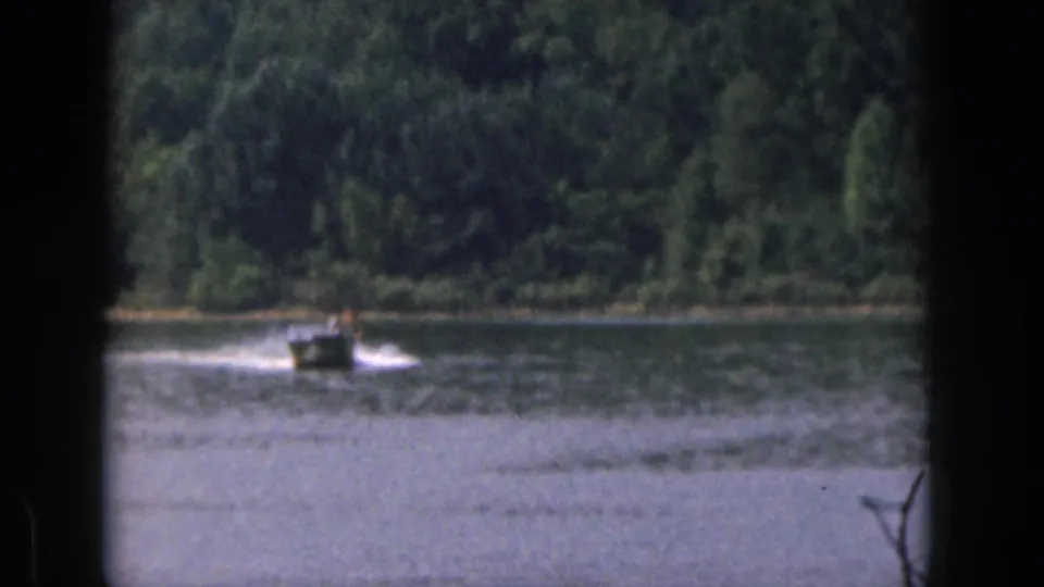 1961 Michigan home-movie frame showing a small motorboat moving across the lake, likely towing the skier outside the frame.
