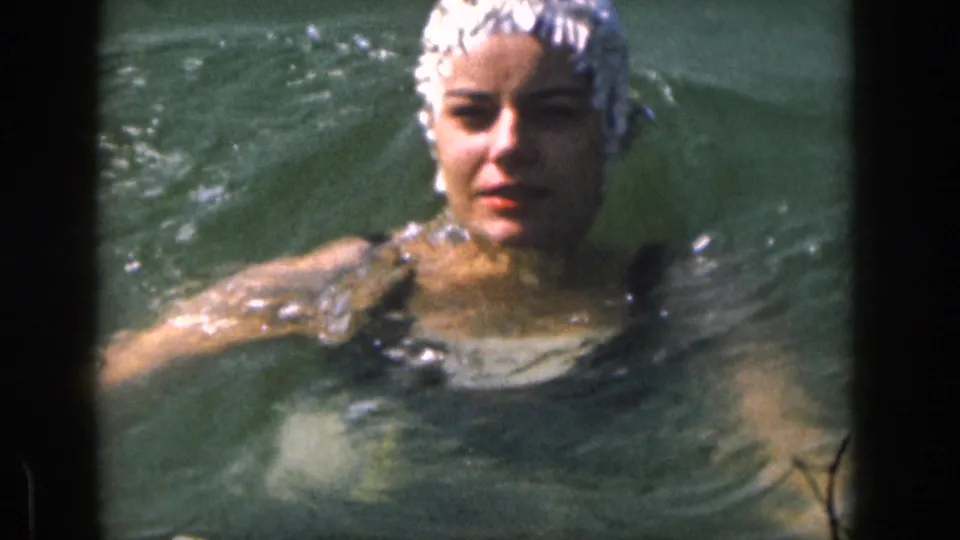1961 Michigan home-movie frame of a woman wearing a swim cap swimming close to the camera in lake water.