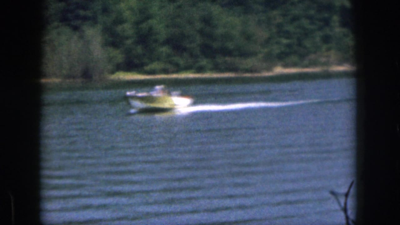 1961 Michigan 8mm frame showing a small motorboat pulling across blue lake water near trees on the far shore.
