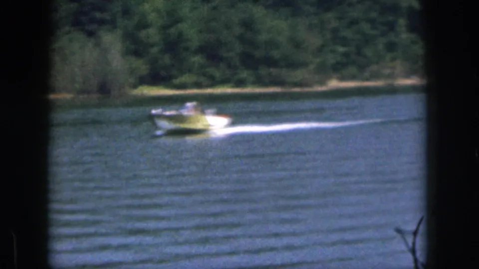 1961 Michigan 8mm frame showing a small motorboat pulling across blue lake water near trees on the far shore.