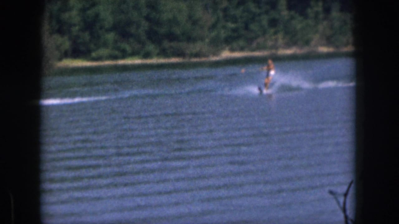 Water skier at distance being pulled across a lake with spray behind.