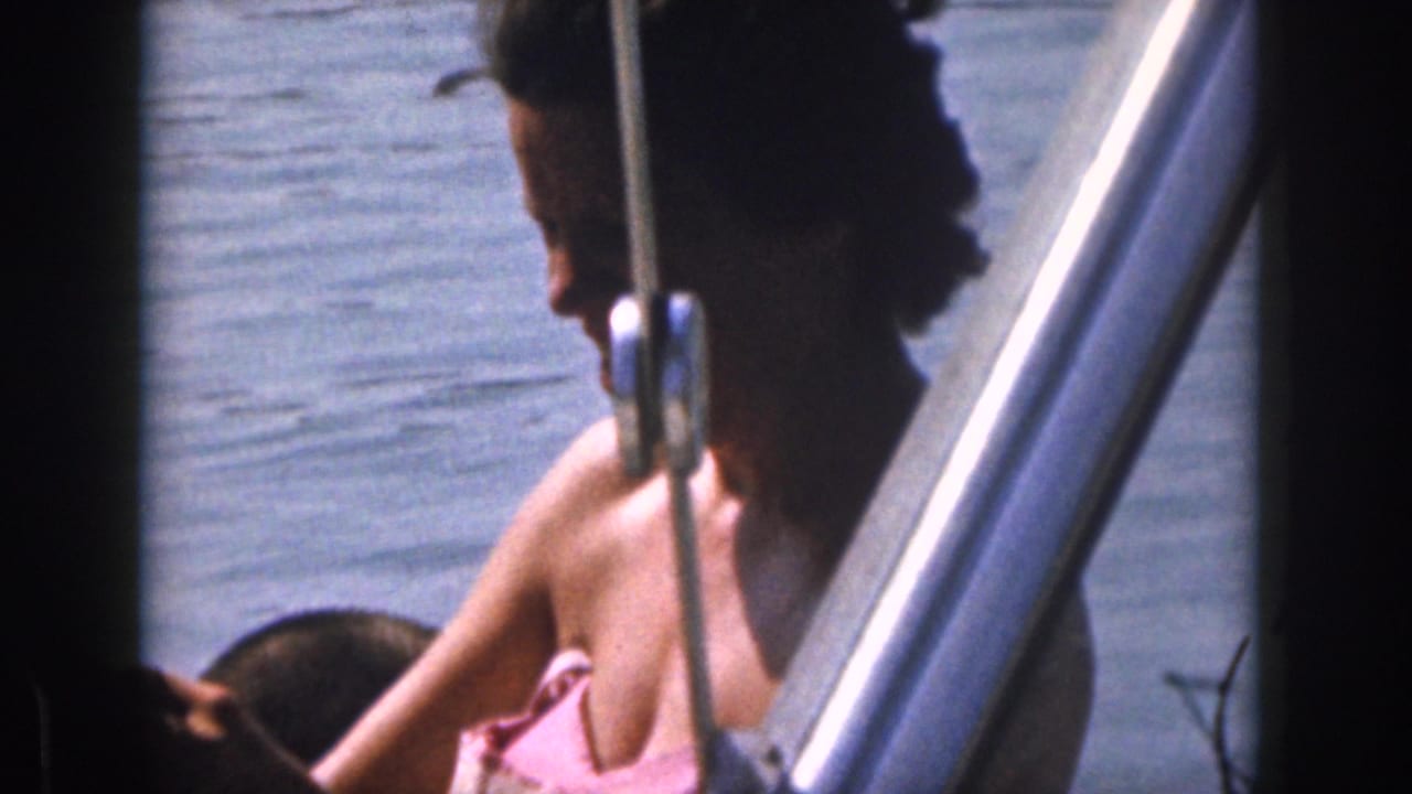1961 Michigan 8mm frame showing boat passengers on lake water, with a woman in a pink swimsuit partly framed by boat hardware.
