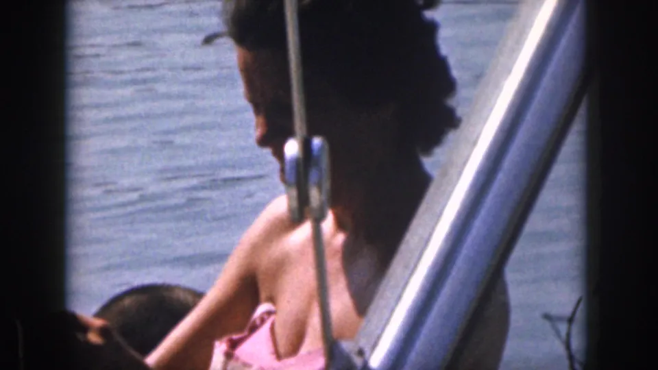 1961 Michigan 8mm frame showing boat passengers on lake water, with a woman in a pink swimsuit partly framed by boat hardware.