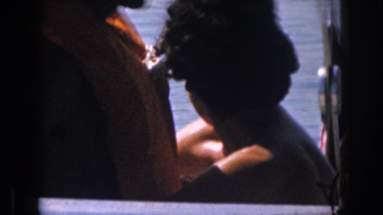 1961 Michigan home-movie frame with partially silhouetted passengers seated on a boat, lake water behind them.