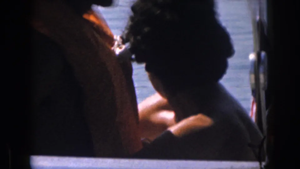 1961 Michigan home-movie frame with partially silhouetted passengers seated on a boat, lake water behind them.