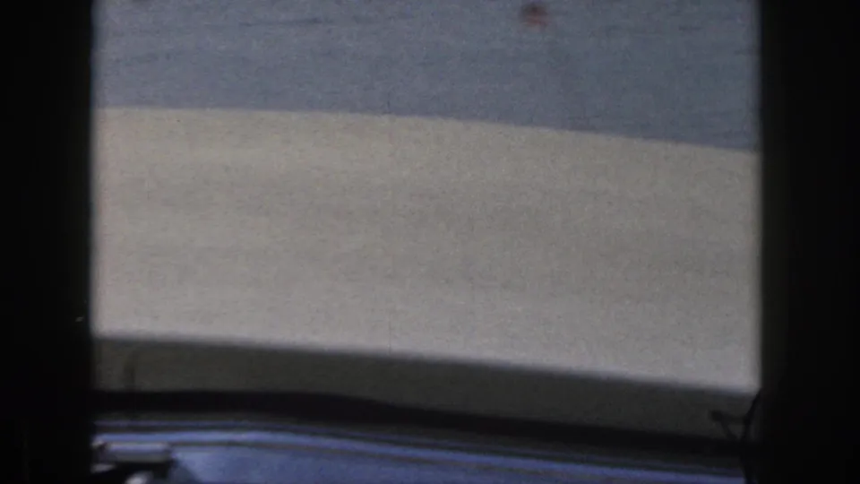 A soft, partially obstructed lake view shows water, distant shoreline, and the dark edge of a window frame in 1961 Michigan footage.