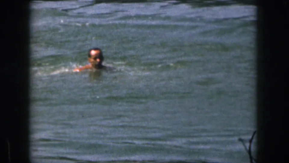 A swimmer faces the camera while treading water in choppy Michigan lake waves in this 1961 home-movie frame.