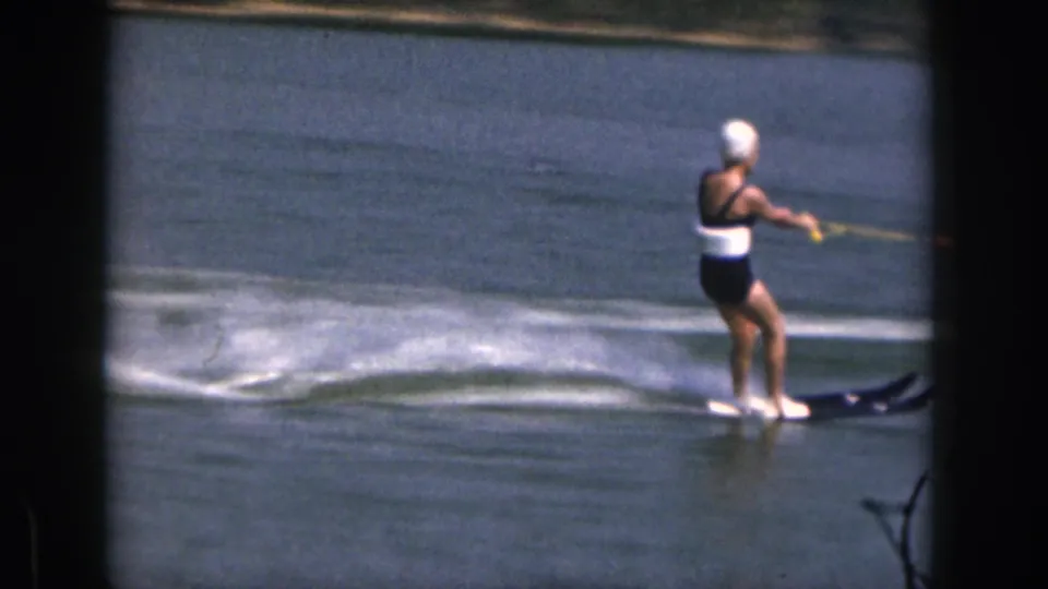 A woman in swimwear water skis across a Michigan lake, holding a tow rope as white wake spreads behind her.